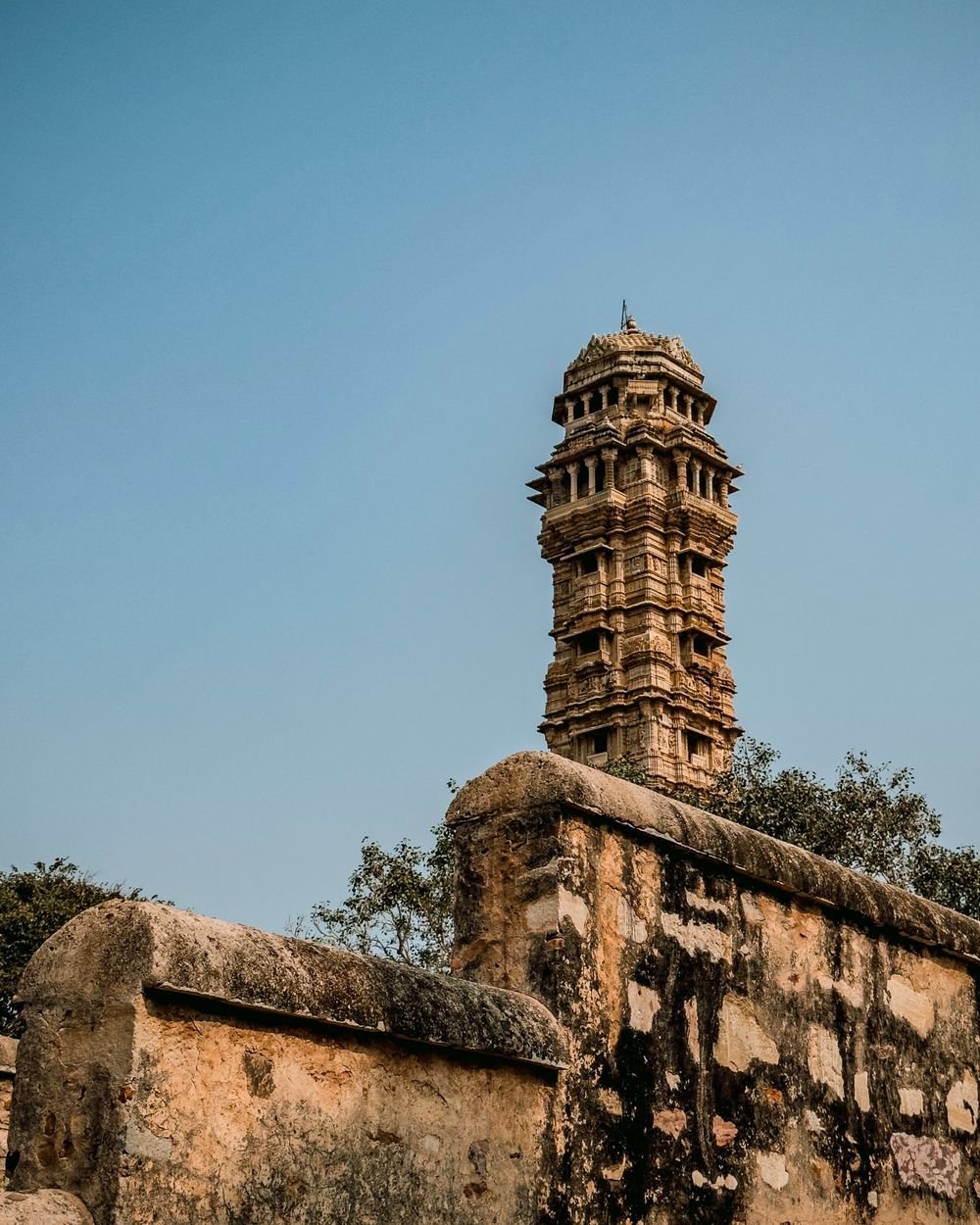 Carved upper storeys of Vijay Stambh rising above a stone wall at Chittorgarh