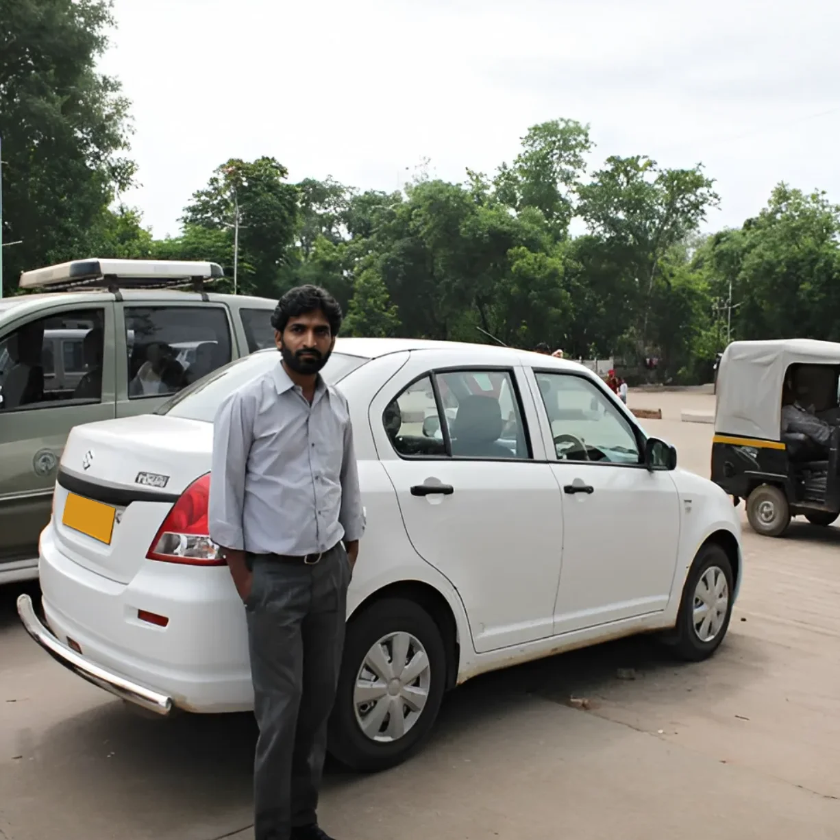 White Maruti Suzuki Swift Dzire with a driver, rear three quarter view