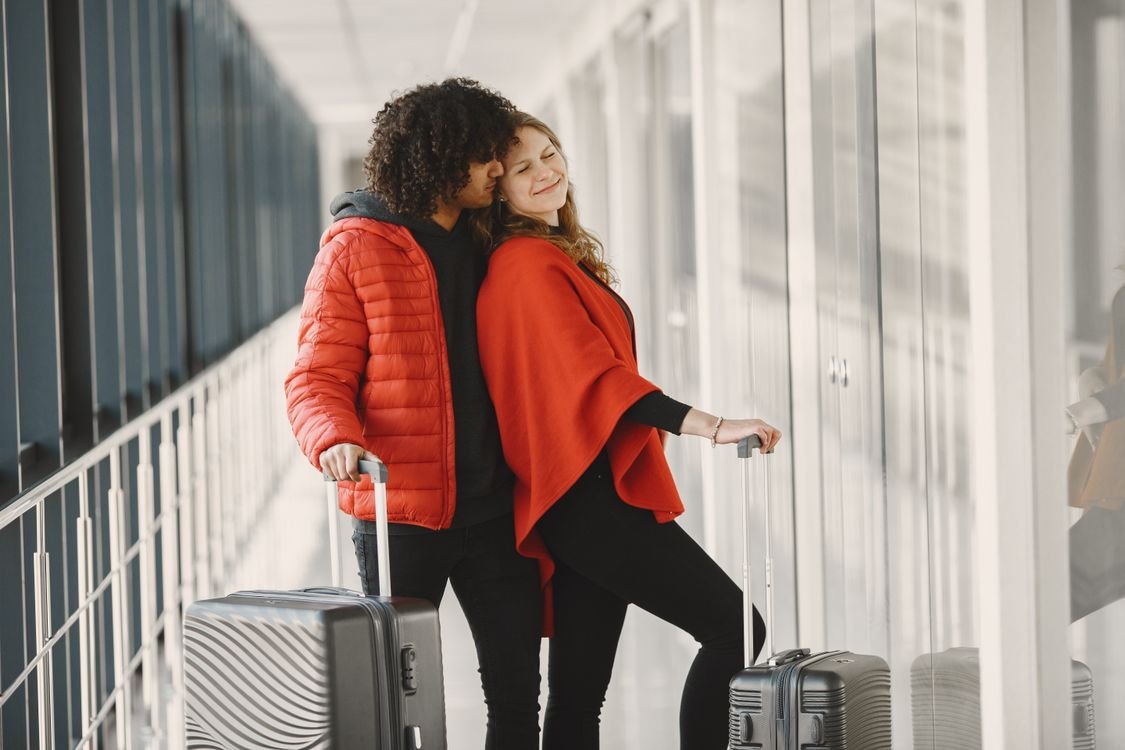 Two travellers with rolling suitcases in an airport corridor