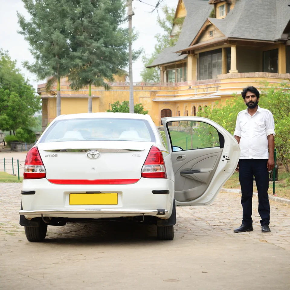 White Toyota Etios with a driver beside the open passenger door