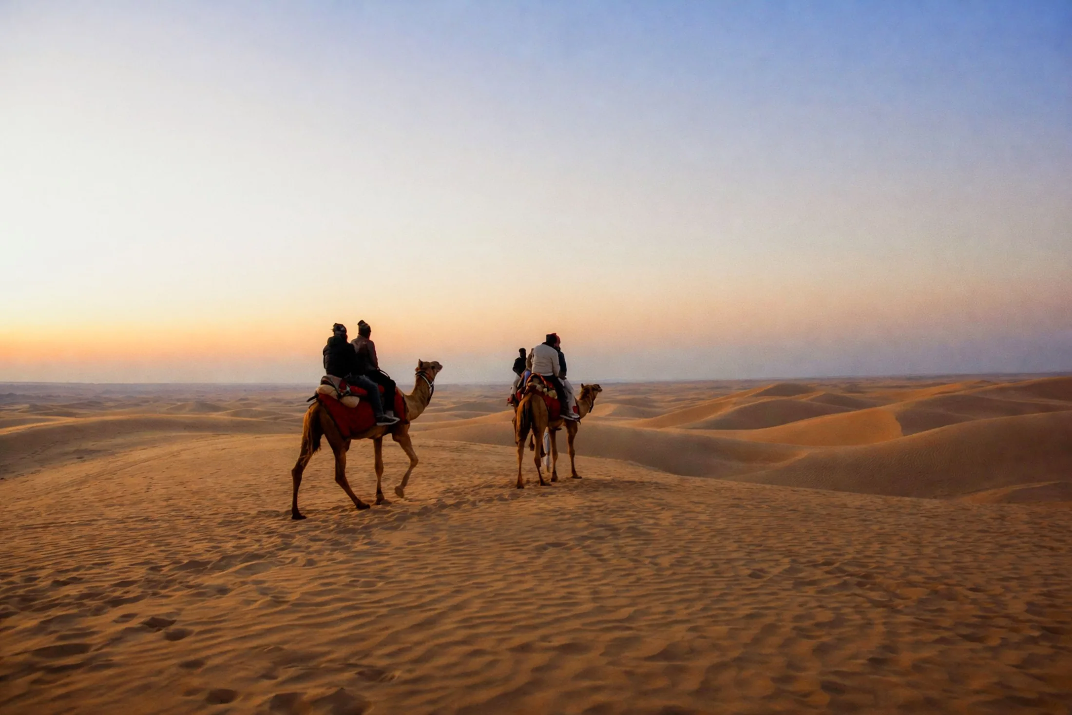 Camel riders crossing the Jaisalmer dunes at sunset